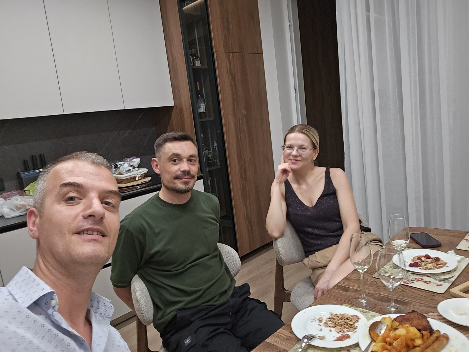 Wide dinner-table photo with smiling people and a cozy kitchen background.